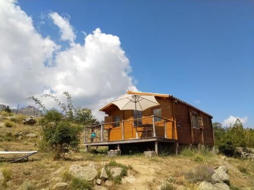 Chalet en bois orange avec terrasse et parasol à Calacuccia, entouré de montagnes et paysage verdoyant sous ciel bleu