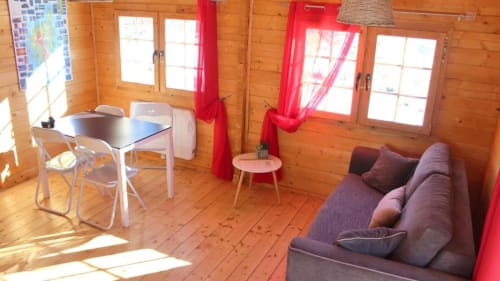 Intérieur du chalet en bois avec canapé violet, table à manger, rideaux rouges et fenêtres aux Chalets de Lozzi, Calacuccia