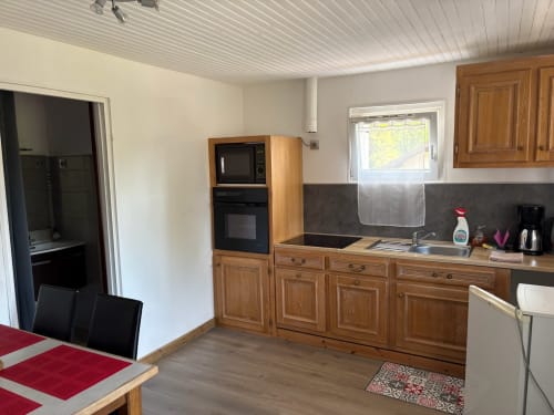 Cuisine spacieuse du Gîte Maisonnette avec meubles en bois, plan de travail noir et vue sur la montagne au Ménil