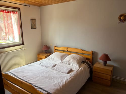 Chambre douillette avec lit en bois, draps blancs et vue sur les montagnes au gîte Les Grandes Voies au Ménil