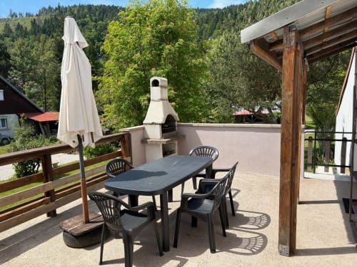 Outdoor terrace dining area at Gîtes les Grandes voies cottage in Le Ménil with forest views, umbrella, and wood pergola