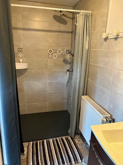 Modern bathroom shower with beige tiles and decorative pattern border at Gîtes Terrasse cottage in Le Ménil, France