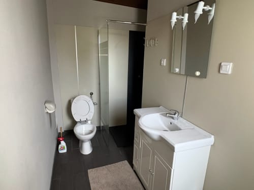 Modern bathroom at Gîtes les Grandes voies cottage with white sink, toilet, mirror, and dark tile flooring in Le Ménil