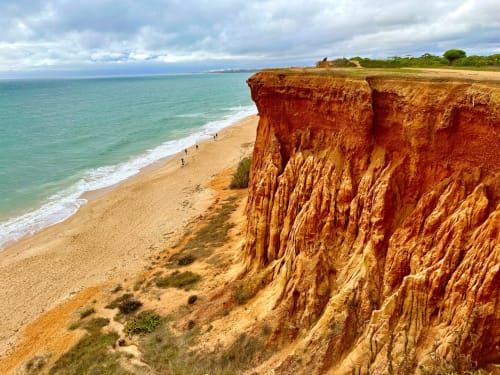 Falésias de arenito vermelho com vista para praia dourada e águas turquesas em Portugal