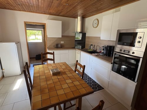 Modern kitchen-dining area in Gîte Jardin cottage with white cabinetry, wooden table, and garden view at Les Grandes voies
