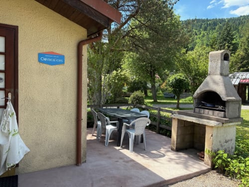 Cottage patio with dining table and stone fireplace, surrounded by green forest at Gîtes les Grandes voies, Le Ménil