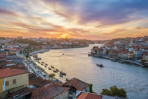 Pôr do sol sobre o Rio Douro no Porto com edifícios coloridos e barcos, Férias Intemporais