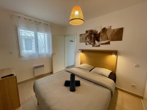 Bright beachside apartment bedroom at Résidence Marina di Bravone with wooden headboard, pendant light, and modern amenities