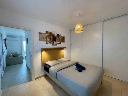 Modern bedroom at Résidence Marina di Bravone with queen bed, wooden headboard, pendant light, and open living area access