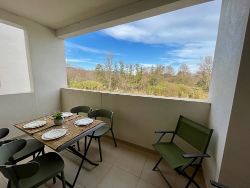 Balcony dining area at Résidence Marina di Bravone with forest views, table set for two, green chairs
