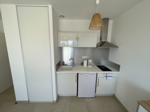 Piccola cucina moderna presso la Résidence Marina di Bravone con mobili bianchi, piano lavoro in acciaio inossidabile, piano cottura e lavello