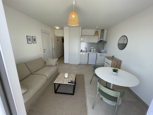 Monolocale moderno a Marina di Bravone con divano beige, angolo cottura, tavolo da pranzo e lampada sospesa intrecciata