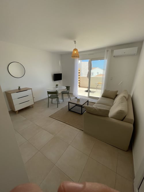 Soggiorno moderno di monolocale a Marina di Bravone con divano beige, zona pranzo e accesso a balcone con vista mare