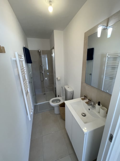 Bagno moderno con vanità bianca, specchio, toilette, cabina doccia e scaldasalviette alla Résidence Marina di Bravone