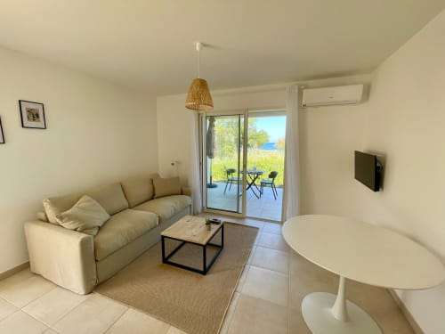 Monolocale moderno a Marina di Bravone con vista sul mare, divano beige, tavolo rotondo e accesso alla terrazza affacciata sulla spiaggia