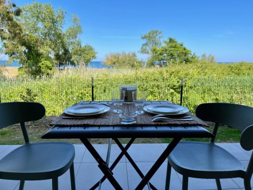 Zona pranzo all'aperto presso la Résidence Marina di Bravone con vista mare, sedie nere e tavolo sulla terrazza con affaccio sulla spiaggia