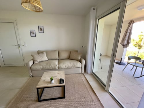 Luminoso soggiorno monolocale della Residenza Marina di Bravone con divano beige, tavolo in legno, tappeto intrecciato e vista sul mare