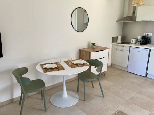 Area pranzo di monolocale moderno con tavolo rotondo bianco, sedie verdi e angolo cottura fronte mare a Marina di Bravone