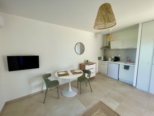 Moderno monolocale a Marina di Bravone con zona pranzo, sedie verdi, cucina bianca, TV e lampade a sospensione in vimini