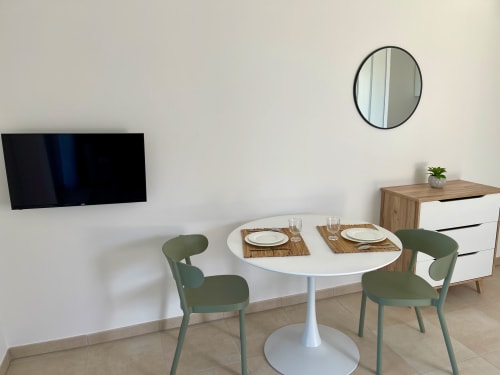 Zona pranzo moderna dello studio Marina di Bravone con tavolo rotondo bianco, sedie verdi, TV a parete e specchio circolare