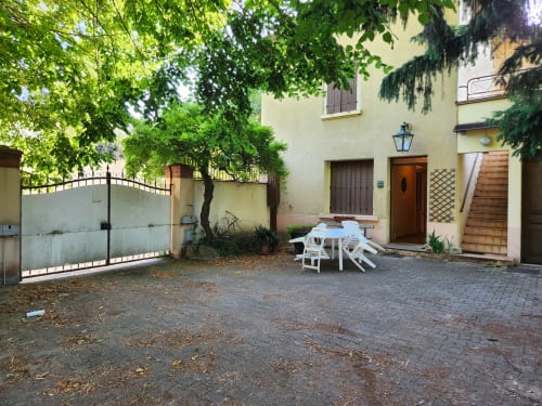 Charmante cour de villa à Charly avec mobilier de patio blanc, verdure luxuriante, portail métallique et façade en pierre jaune