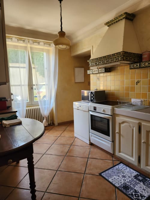 Cuisine spacieuse de villa française avec armoires crème, électroménagers blancs, dosseret en carrelage jaune, sols en terre cuite et jardin