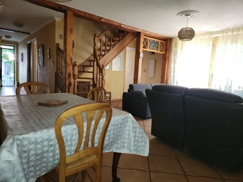 Villa spacieuse avec salle à manger et séjour, escalier en bois, table, chaises, canapé noir et vue sur le jardin à Charly