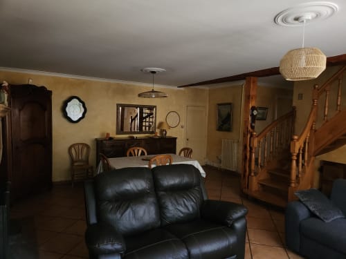 Spacieux séjour de villa avec canapé en cuir noir, table à manger en bois, escalier et murs jaunes à Charly