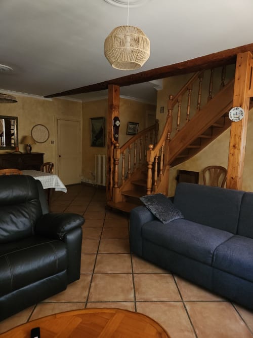 Spacieux salon de villa à Charly avec escalier en bois, fauteuil cuir noir, canapé bleu marine, carrelage terre cuite et tissu tissé