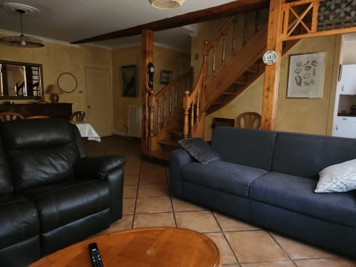Spacieux salon de villa à Charly avec escalier en bois, fauteuil cuir noir, canapé bleu marine, table bois et terracotta