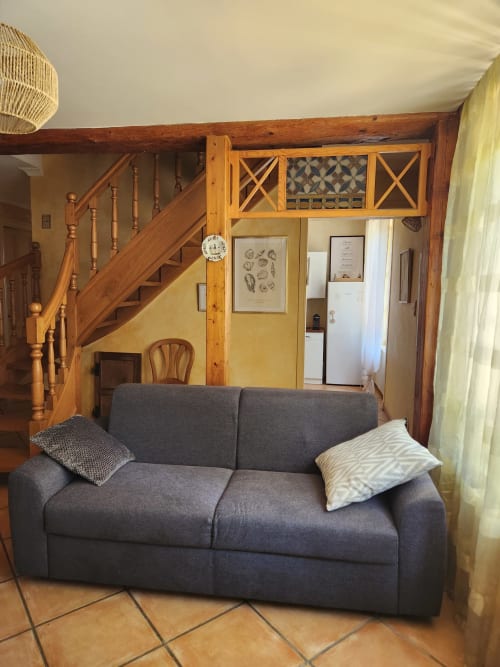 Salon cozy avec canapé gris, escalier en bois et mur jaune dans une villa française avec vue sur le jardin