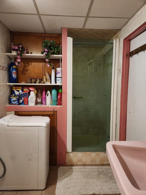 Salle de bain dans villa française avec baignoire rose, lave-linge blanc, étagère rose avec produits de toilette et douche verte
