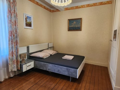 Chambre moderne de la villa Charly avec lit noir, tête de lit blanche, parquet et vue sur le jardin à travers les rideaux à fleurs