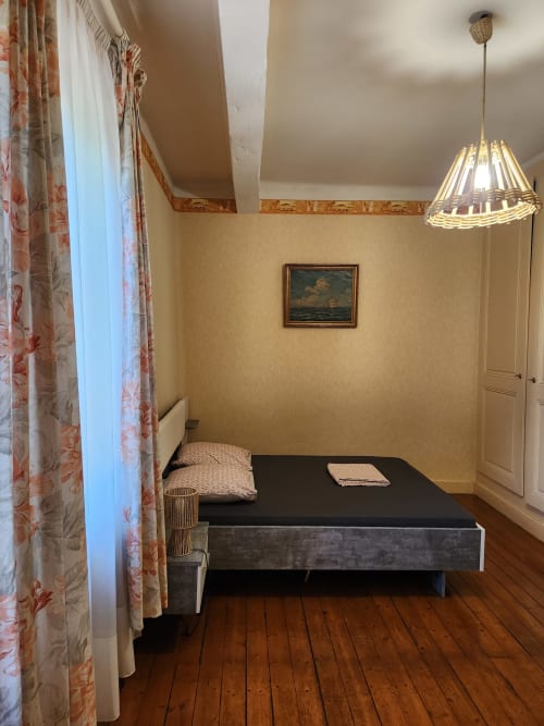 Chambre confortable de la villa Charly avec lit simple, parquets, rideaux fleuris, lampe suspendue et tableau encadré