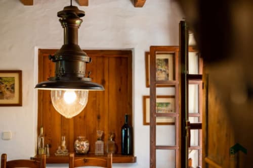 Lámpara colgante rústica con pantalla de cristal sobre estantería de madera con botellas en el hotel Barrosa Home, España