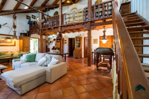 Sala rústica Barrosa Home con vigas de madera vista, suelos de terracota, entrepuente de madera y sofá crema