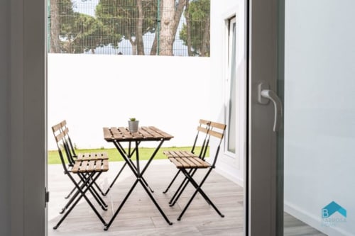 Patio exterior de Barrosa Home con sillas de madera, mesita y maceta con vista al jardín verde