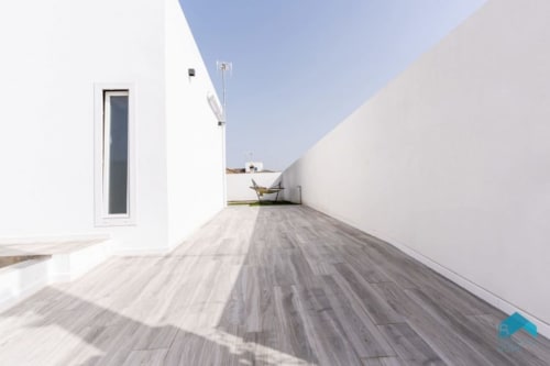 Moderna terraza en la azotea de Barrosa Home con deck de madera gris, paredes blancas y silla de descanso