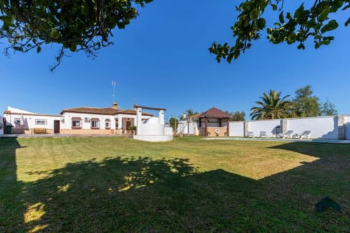 Propiedad Barrosa con edificios blancos, jardín cuidado, palmeras y cielo azul despejado en España