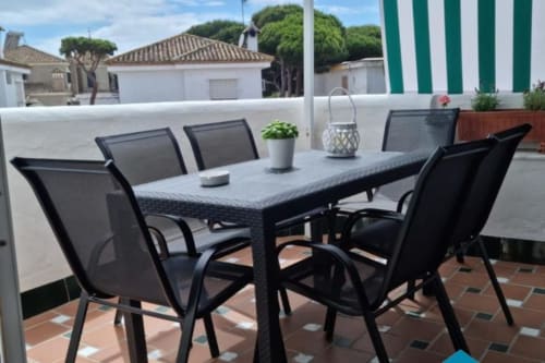 Área de comedor en azotea de Barrosa Home con muebles de patio negro, baldosas de terracota y edificios blancos mediterráneos