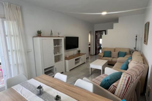 Sala moderna en Barrosa Home con sofá seccional beige, TV de pantalla plana, unidad de almacenamiento blanca e iluminación natural