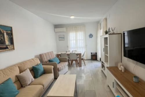 Sala de estar abierta Barrosa Home con sofá beige, comedor, TV de pantalla plana y decoración costera en España