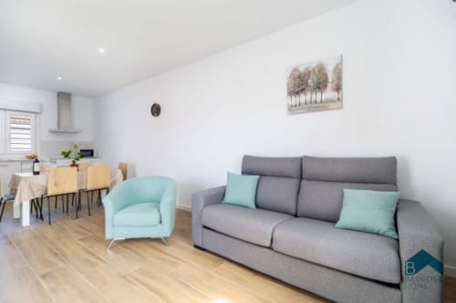Modern living room at Barrosa Home with gray sofa, turquoise armchair, and dining area in open-plan layout