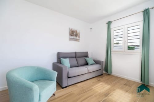 Modern living room at Barrosa Home with gray sofa, turquoise armchair, wooden floor, and green curtains