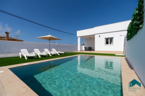 Barrosa Home luxury villa with turquoise pool, white loungers, parasol, and modern white house in Spain