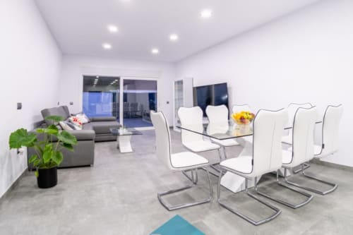 Moderna zona abierta de salón y comedor en Barrosa Home con sillas blancas, sofá gris y decoración contemporánea en España