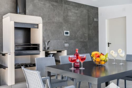 Cocina y comedor moderno en Barrosa Home con paredes de azulejos oscuros, chimenea blanca y frutero sobre mesa negra