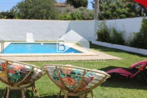 Patio trasero de Barrosa Home con piscina, tumbonas y cerca blanca de privacidad bajo un cielo despejado