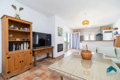 Luminoso salón diáfano en Barrosa Home con muebles de madera, televisor, suelos de terracota y cocina moderna