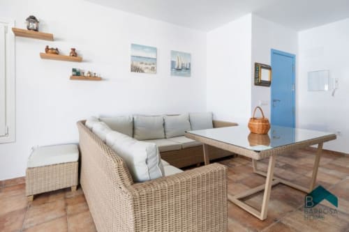 Sala moderna en Barrosa Home con muebles tejidos, cojines grises, mesa de madera y decoración costera en España
